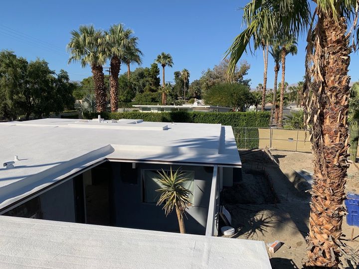 A white flat roof of a house with palm trees in the background under a clear blue sky.