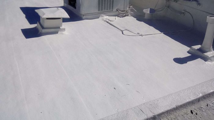 White commercial flat roof with vents and details, casting strong shadows in bright sunlight.