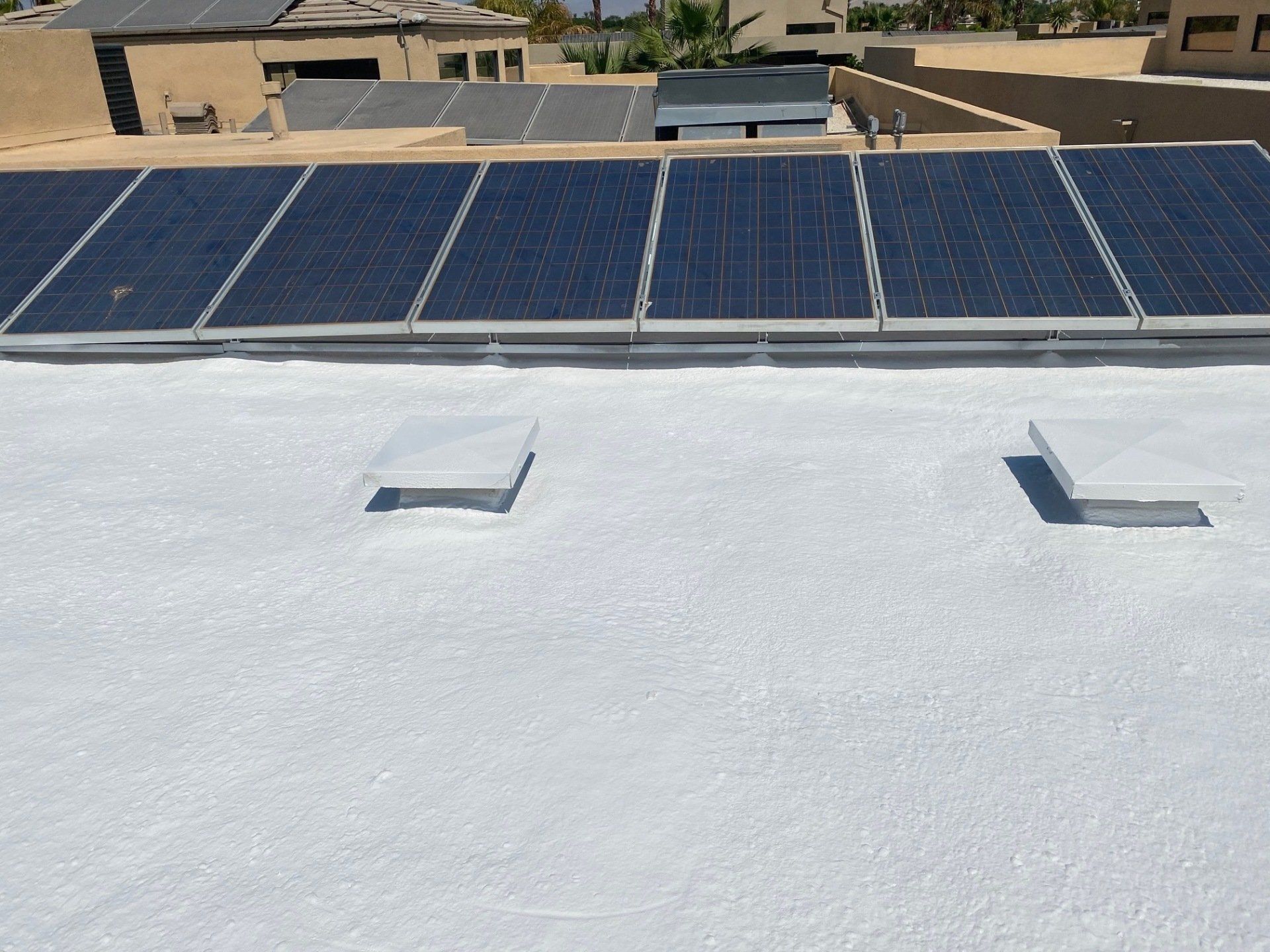 White rooftop with solar panels and two square vents; in an outdoor setting.