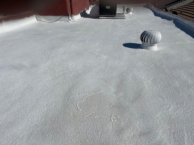 A flat, white roof with a rotary vent and air vent visible. The roof has slight texture and is in sunlight.