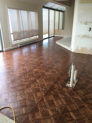Empty room with parquet floor, large windows, and exposed pipes in the foreground.