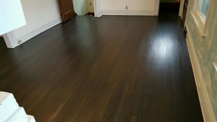Empty room with dark wood floors and light walls, viewed from a corner near a window.