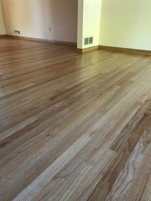 Empty room with wood-look flooring and beige walls, showing a floor vent near the corner.