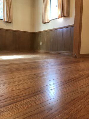 Empty room with wood-paneled walls, hardwood floor, and two curtained windows