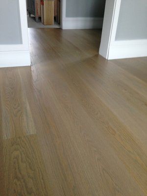Empty hallway with light wood flooring and white walls leading into another room