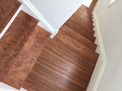 Wooden staircase with reddish-brown steps and white trim in a narrow indoor hallway