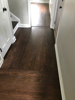 Narrow hallway with dark wood flooring and white walls leading to a bright doorway