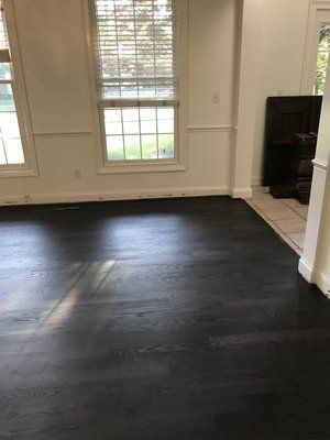 Empty room with black hardwood floor, white walls, and windows letting in daylight