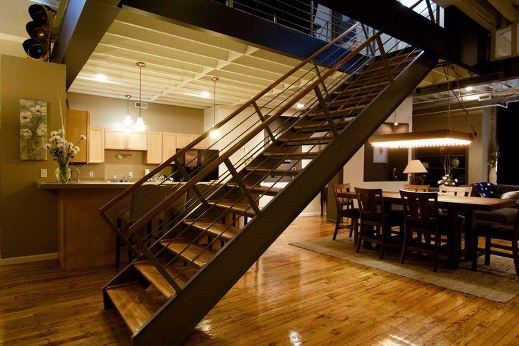 Wooden staircase in a warmly lit loft-style restaurant with dining tables below