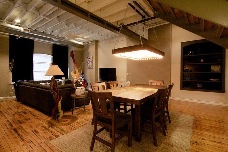 Loft dining area with wooden table, chairs, dark sofa, and hanging light under exposed ceiling beams.