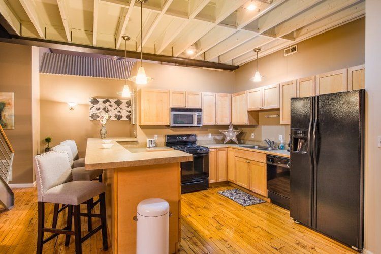 Bright modern kitchen with wood floors, black appliances, and a breakfast bar under a vaulted ceiling