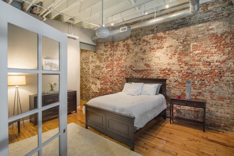 Loft bedroom with exposed brick wall, wooden bed, and glass-paneled door