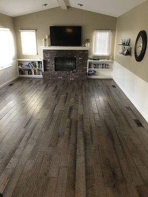 Living room with dark wood floors, brick fireplace, wall-mounted TV, and windows on either side