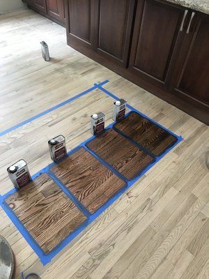 Blue-taped floor grid with four cans on wooden planks beside kitchen cabinets