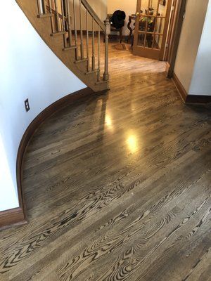 Curved hardwood floor entryway with staircase and hallway railing under warm indoor light