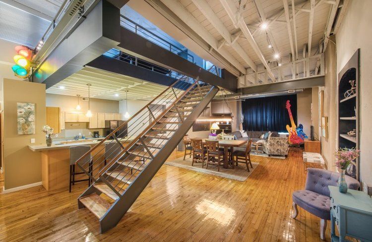 Loft-style open room with wood floors, metal staircase, dining table, and stage area with curtains