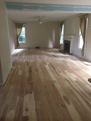 Empty living room with light wood floors, beige walls, curtains, and a fireplace