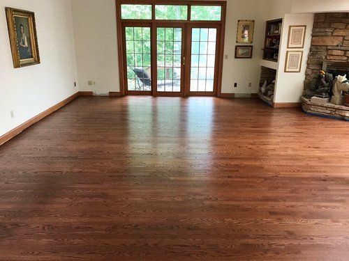 Empty living room with hardwood floors, white walls, a fireplace, and glass doors opening to a green yard