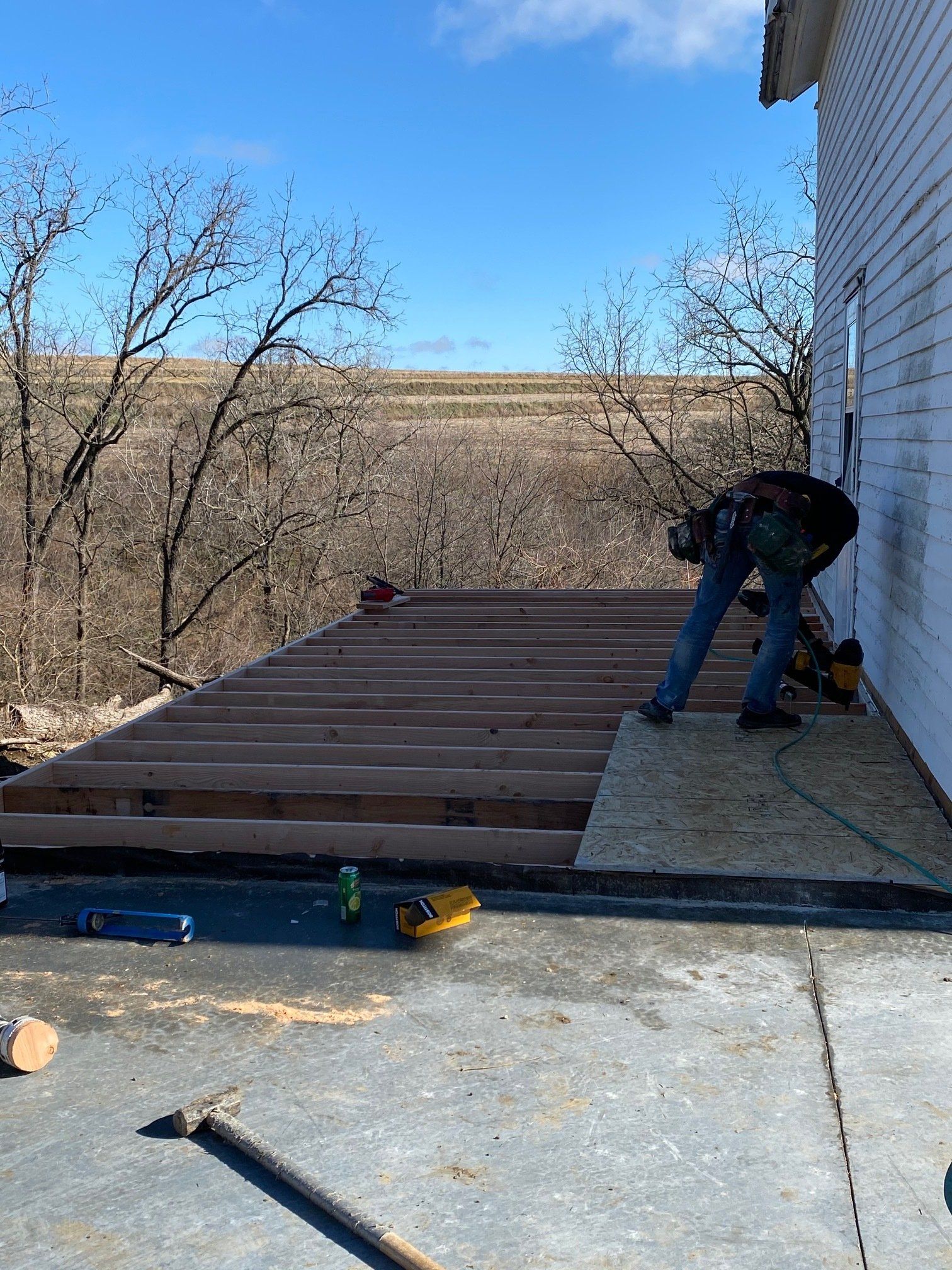 Construction worker building a wood deck on a concrete surface next to a white house.