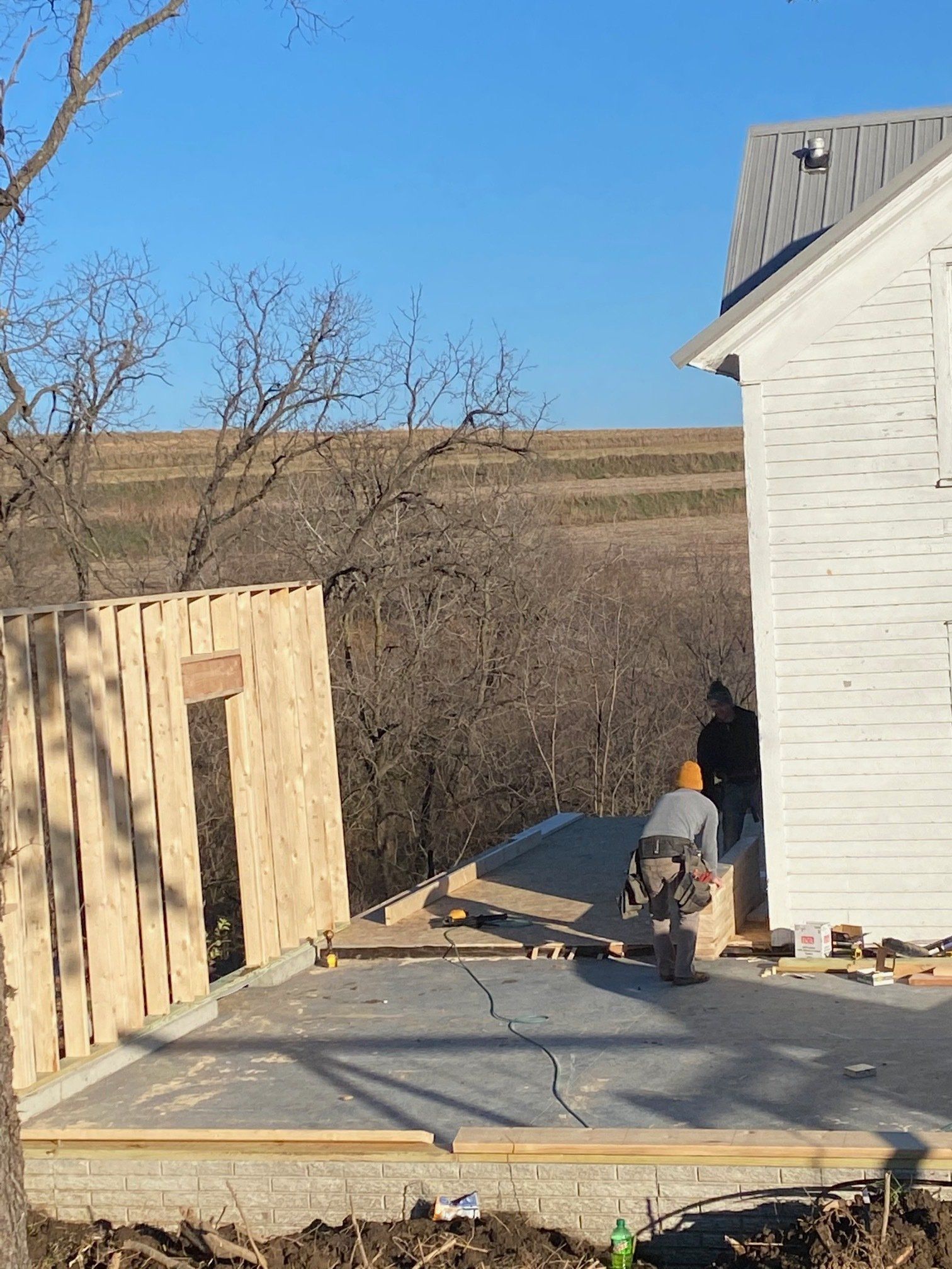Construction workers building a structure near an existing white building, with a blue sky background.
