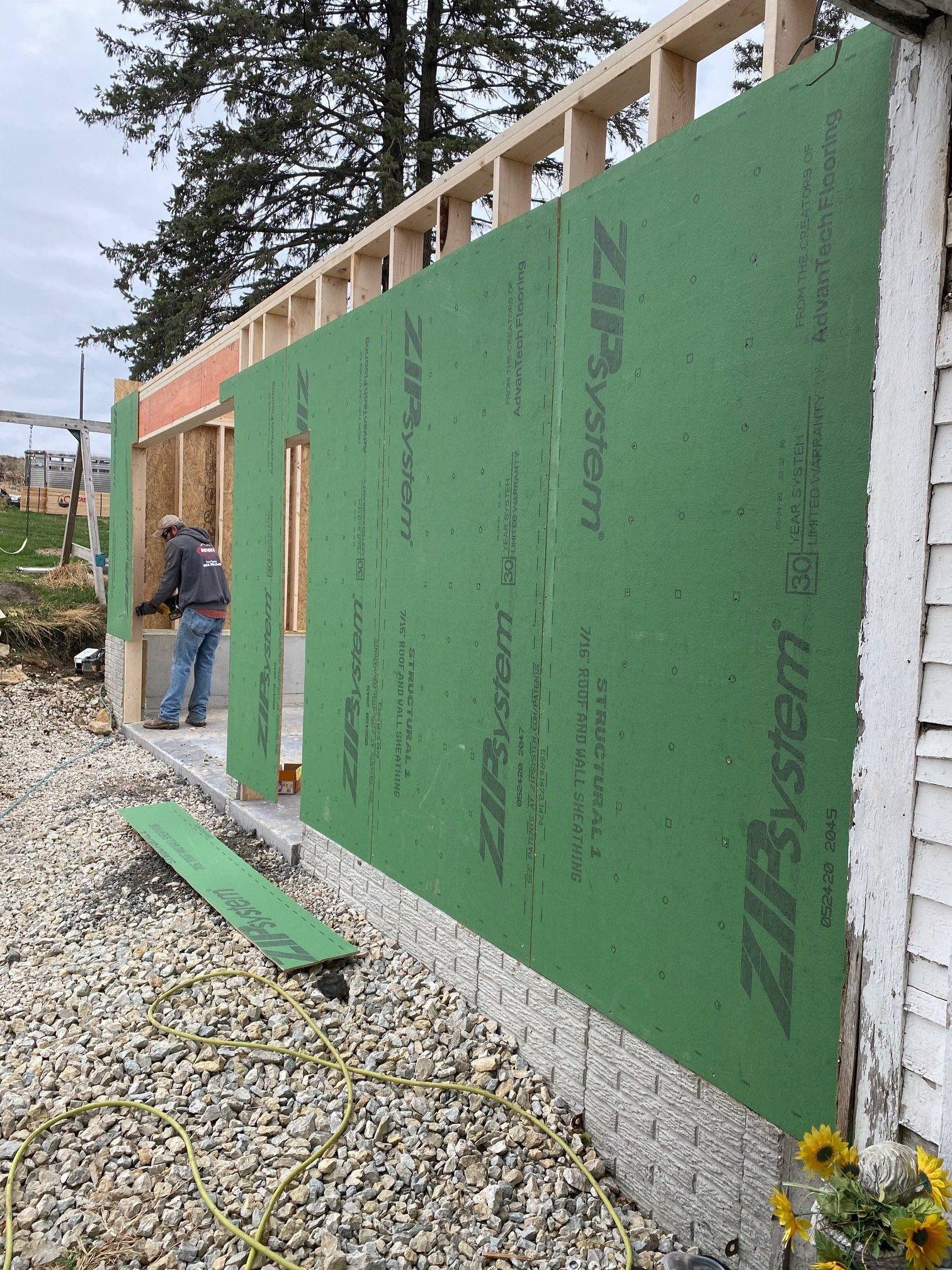 Construction worker installs green siding on a building's exterior wall.