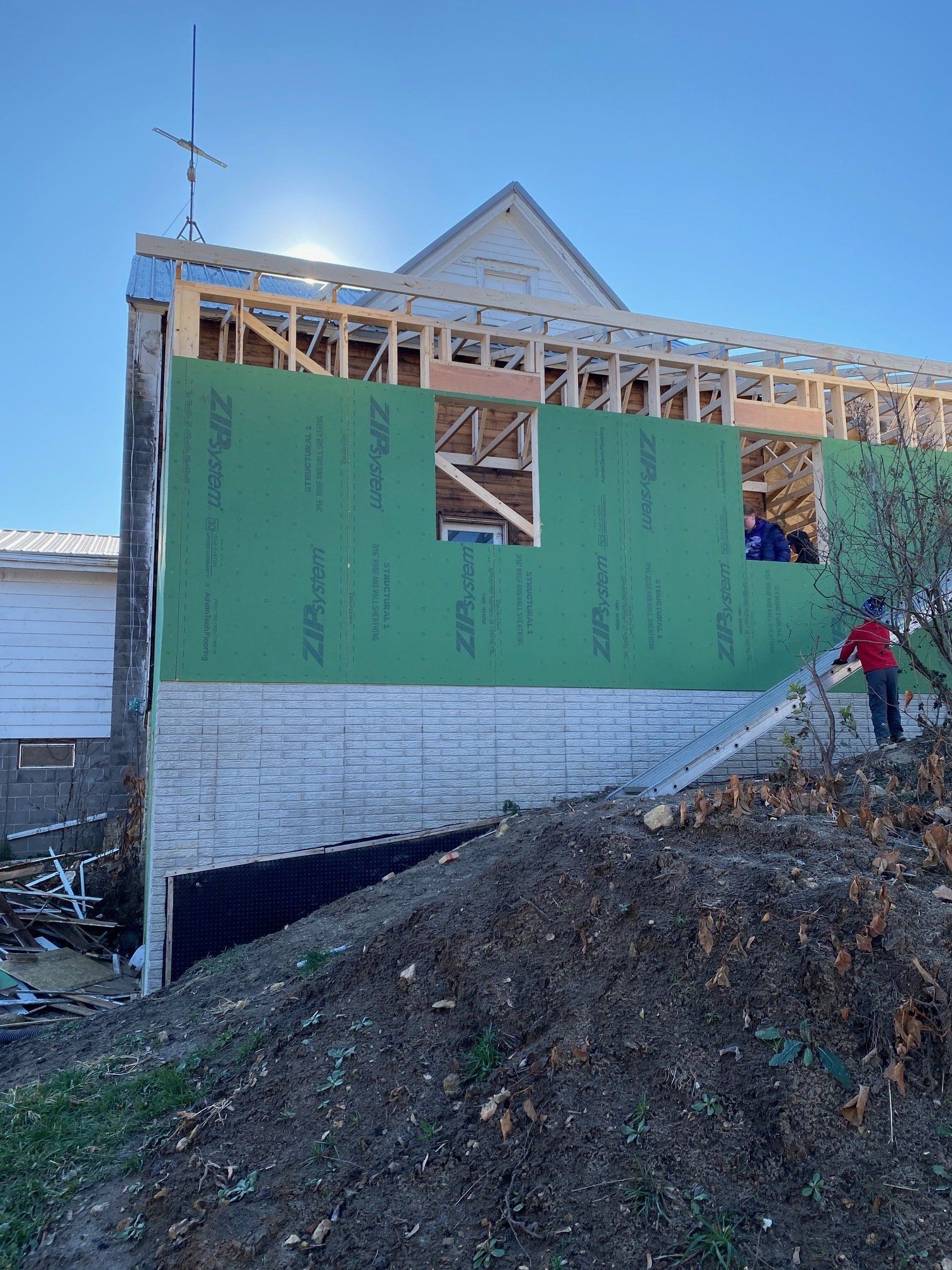 Building under construction, green sheathing, wooden frame, and person on a ladder.