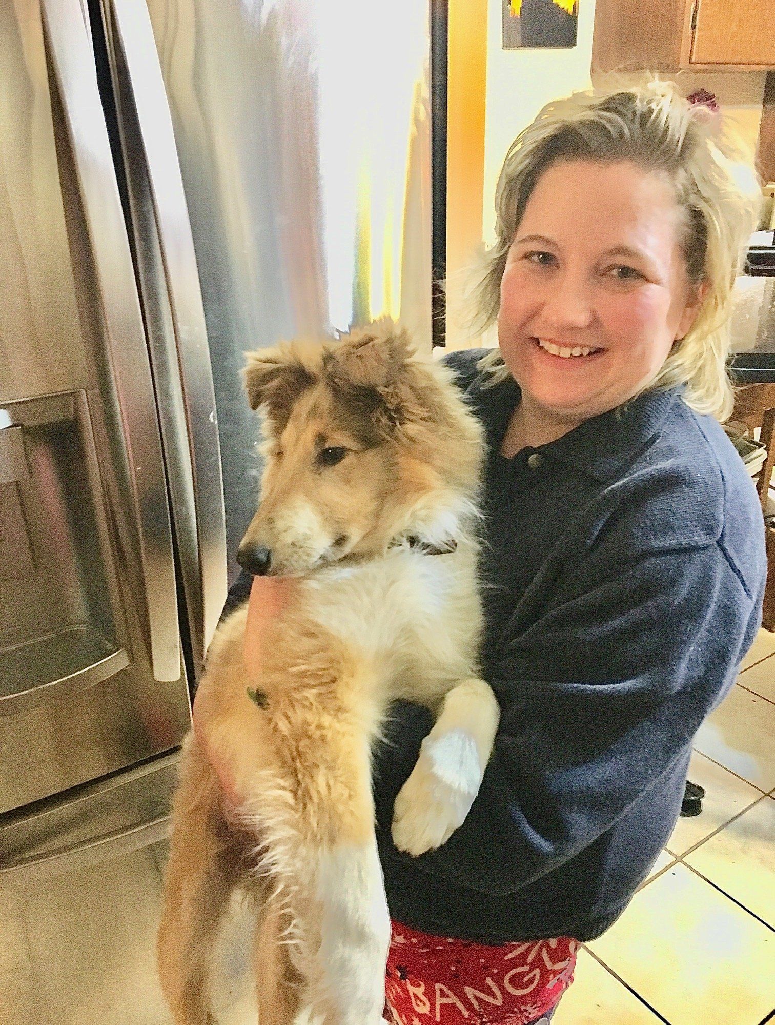 Woman holding a Collie puppy with a bandaged paw, smiling in a kitchen.
