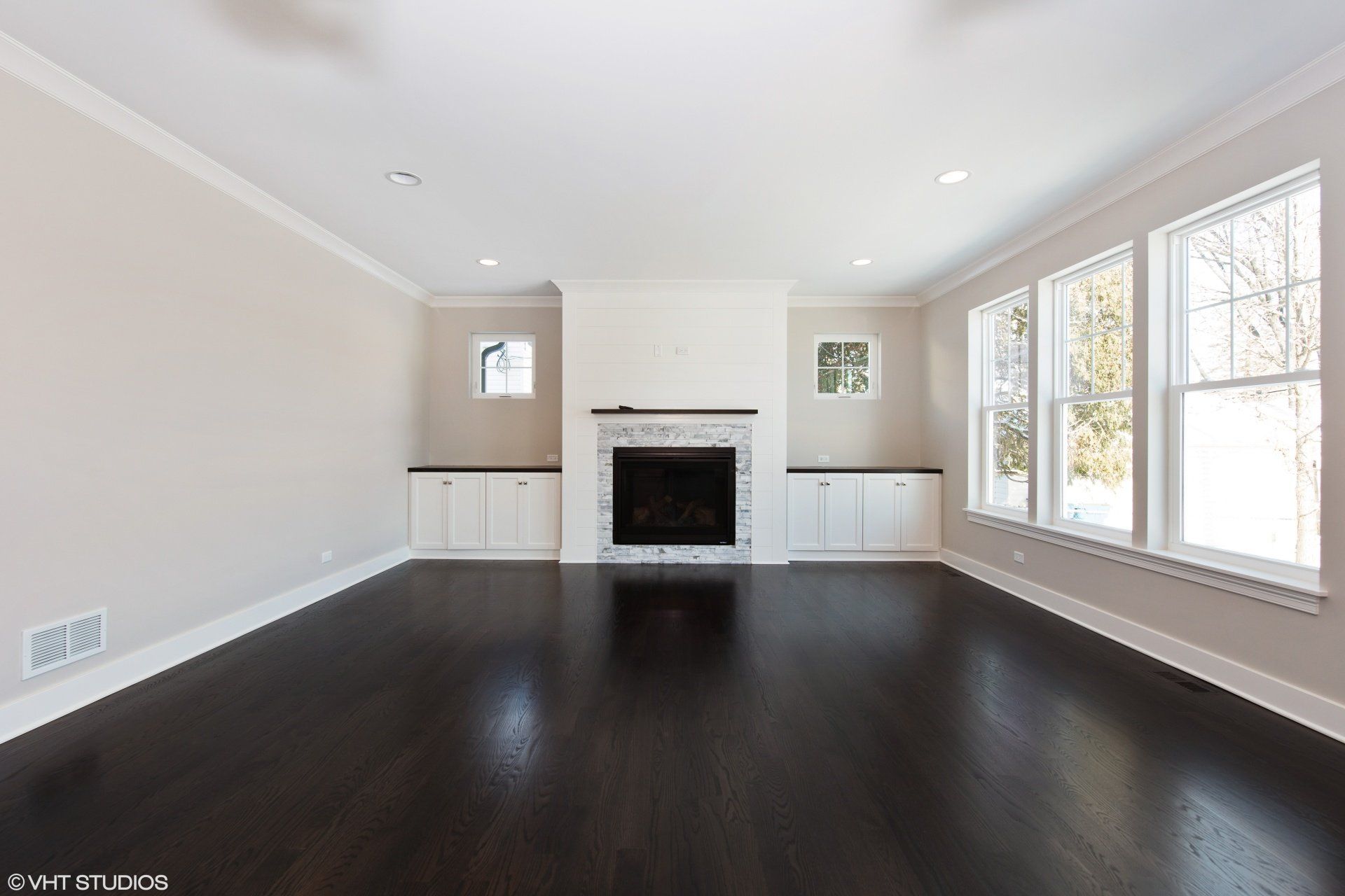 An empty living room with a fireplace and lots of windows.