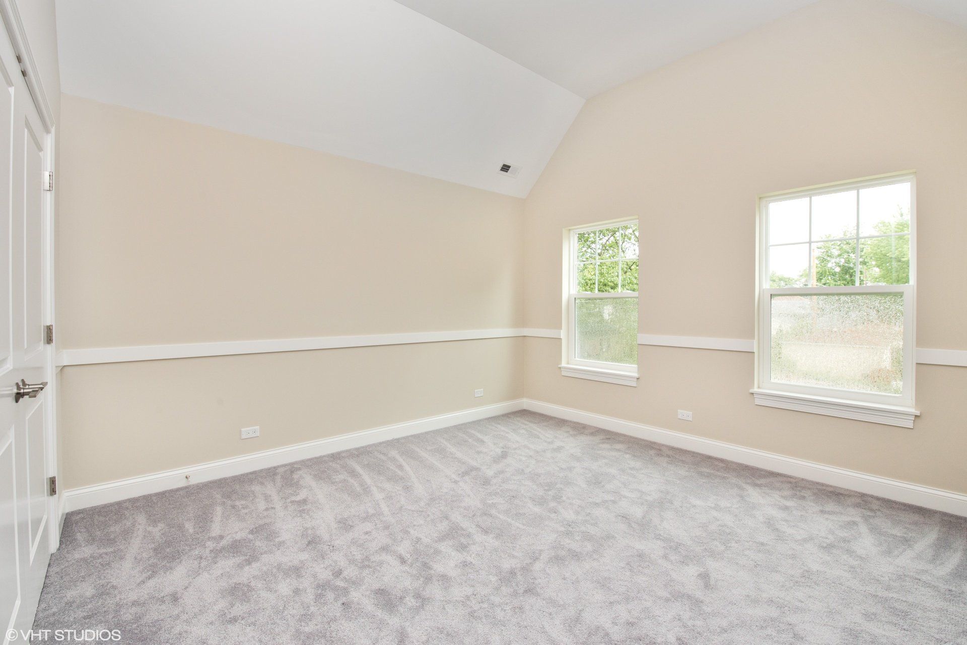 An empty bedroom with two windows and a gray carpet.