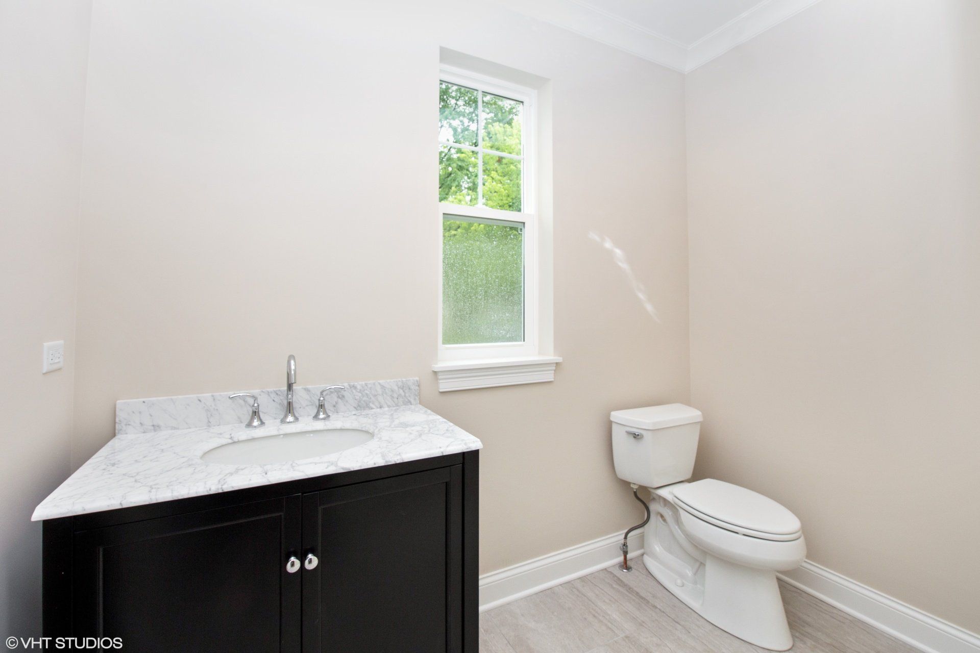 A bathroom with a toilet , sink and window.