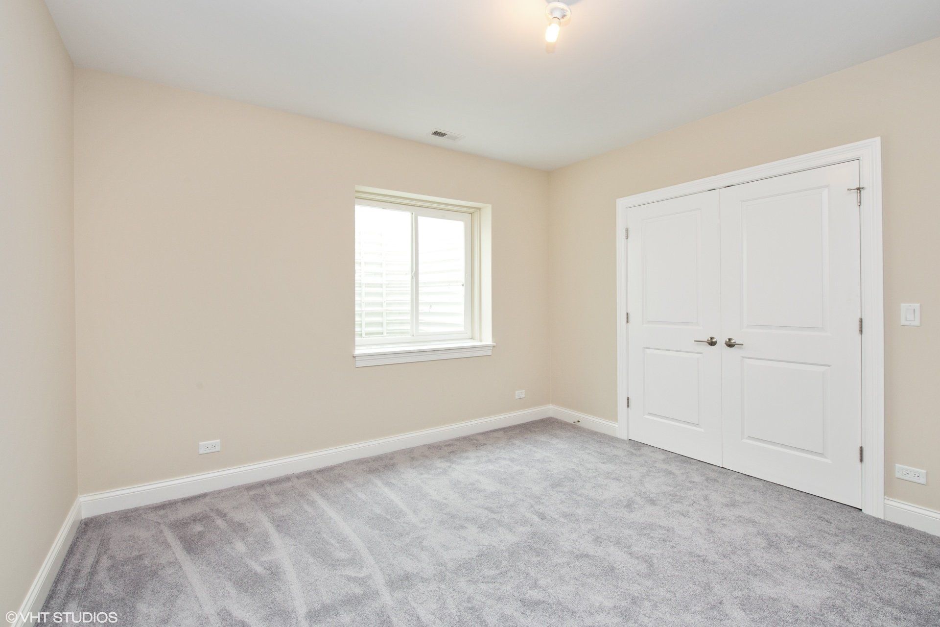 An empty bedroom with a window and a gray carpet.