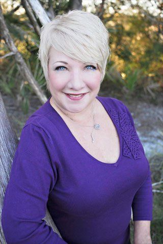 Smiling person in a purple top standing outdoors with trees in the background