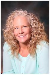 Smiling woman with curly blonde hair wearing a light blue top against a dark background