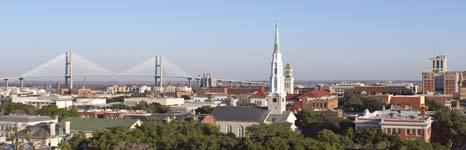 Panoramic city skyline with bridges and a tall white church steeple under a clear blue sky