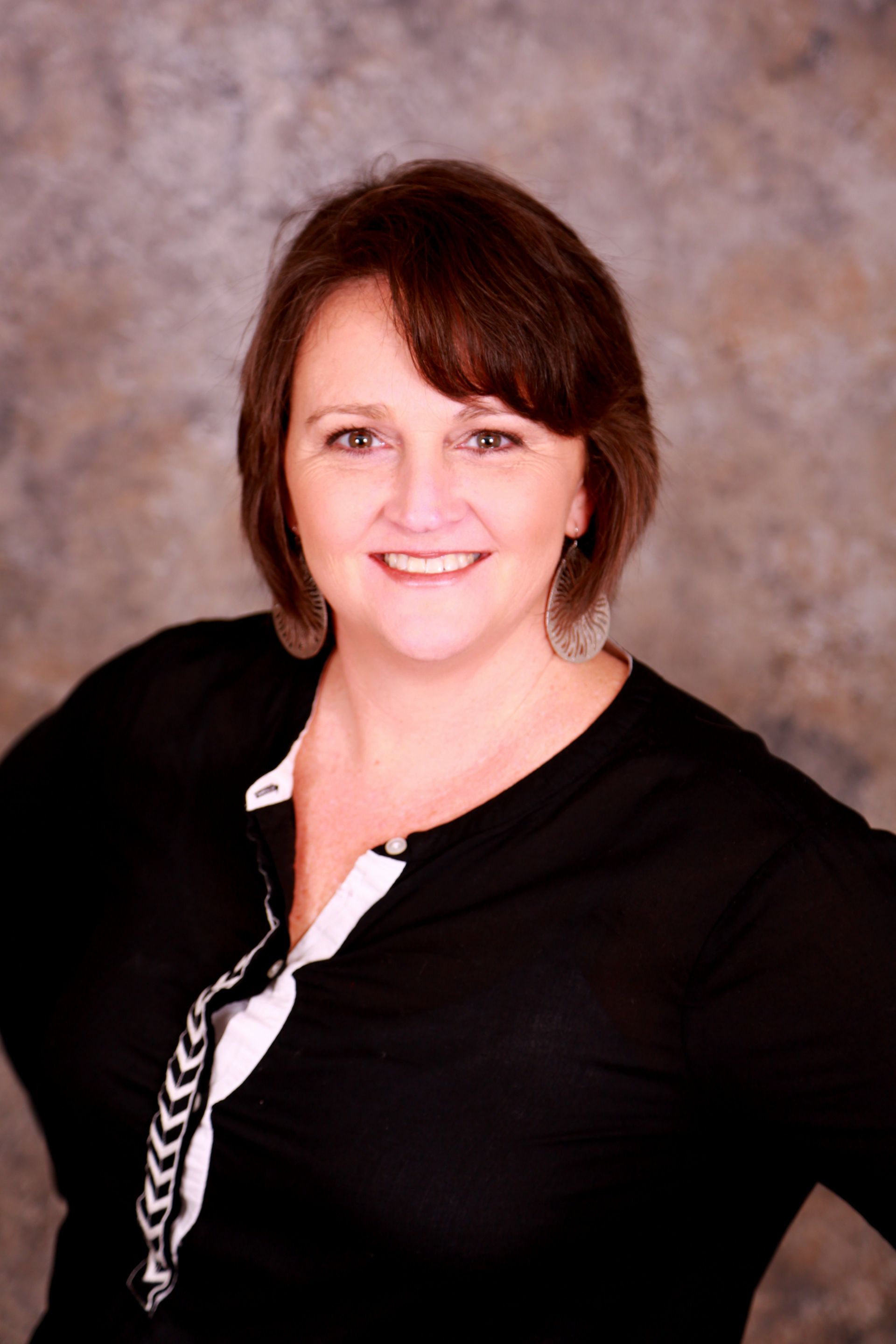 Smiling woman in a black top against a mottled brown studio backdrop