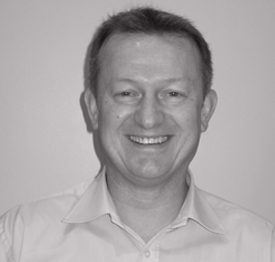 A man in a white shirt is smiling in a black and white photo