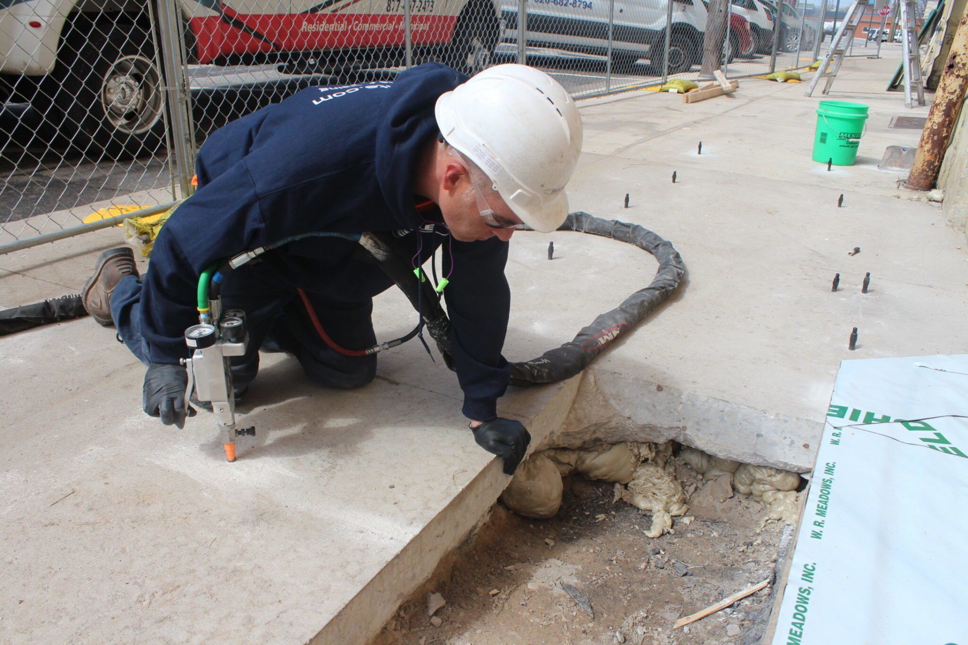 A man wearing a hard hat is working on a sidewalk