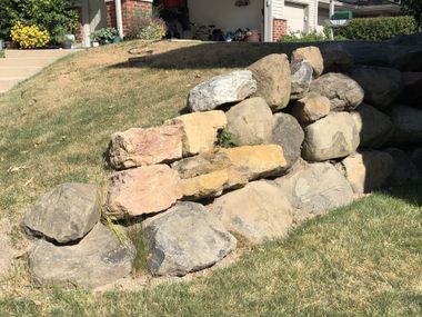 A pile of rocks is sitting in the grass in front of a house.