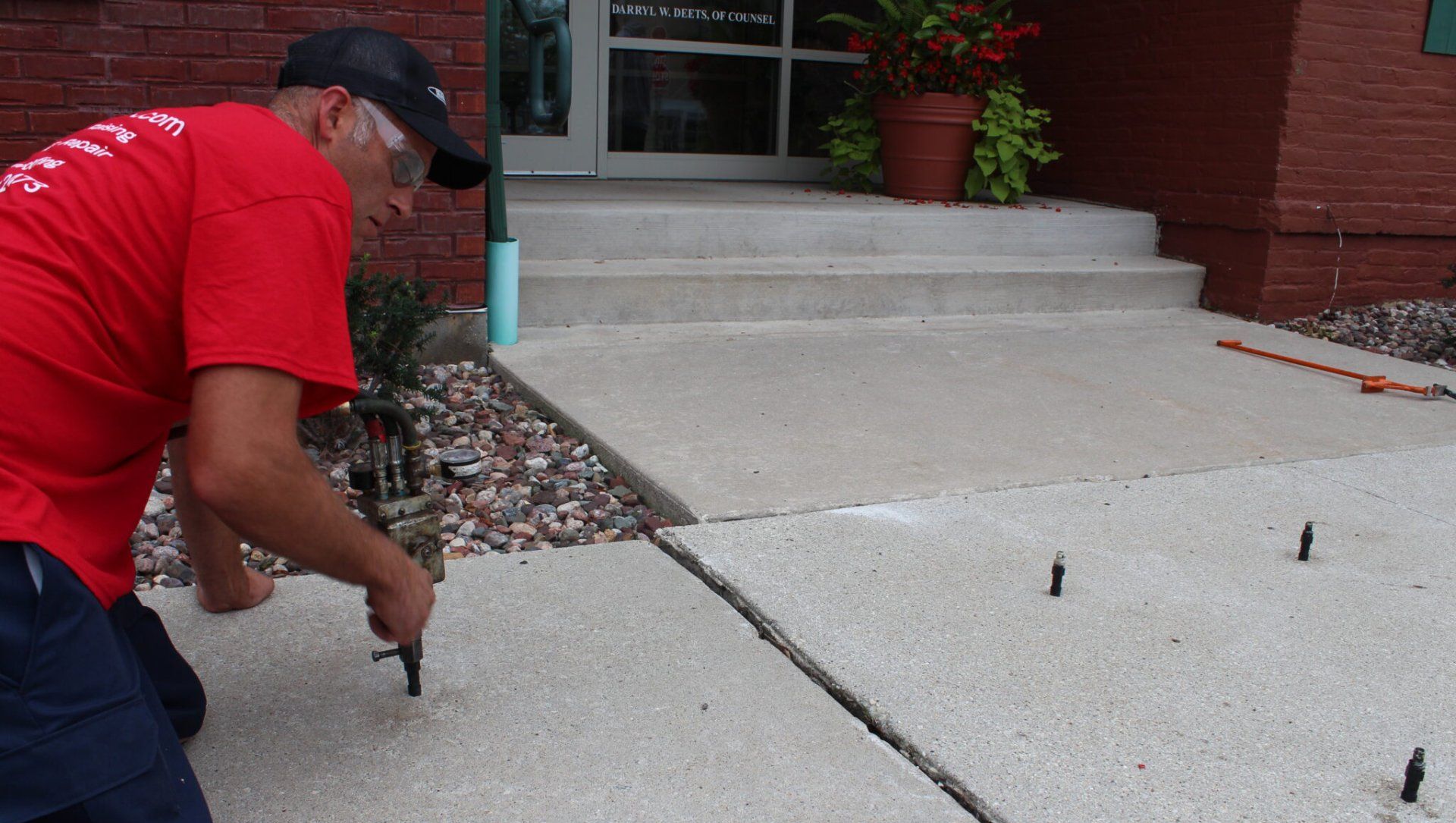 A man in a red shirt is working on a sidewalk.
