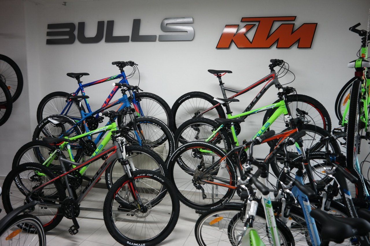 Eine Wand in einem Fahrradladen mit Bulls- und KTM-Logos, davor mehrere Mountainbikes geparkt.