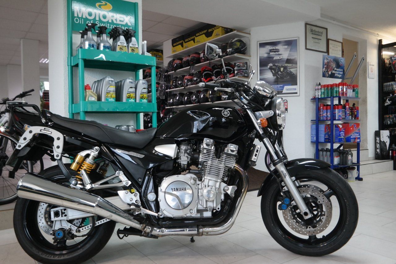 Ein schwarzes Yamaha-Motorrad parkt in einem Geschäft; im Hintergrund sind Regale mit Ölprodukten zu sehen.