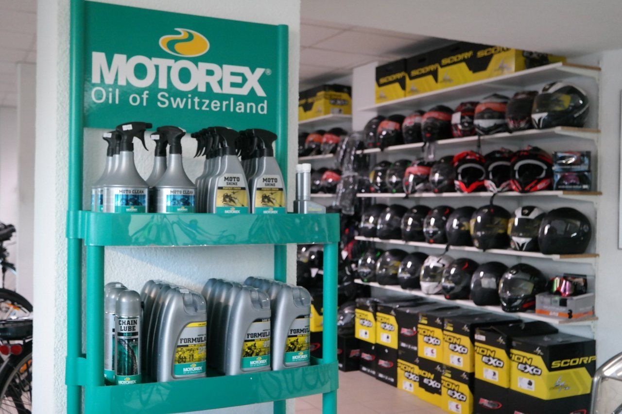 Ein Ladendisplay mit Motorex-Reinigungssprays und -Ölen auf grünen Regalen neben Reihen von Motorradhelmen in Regalen.