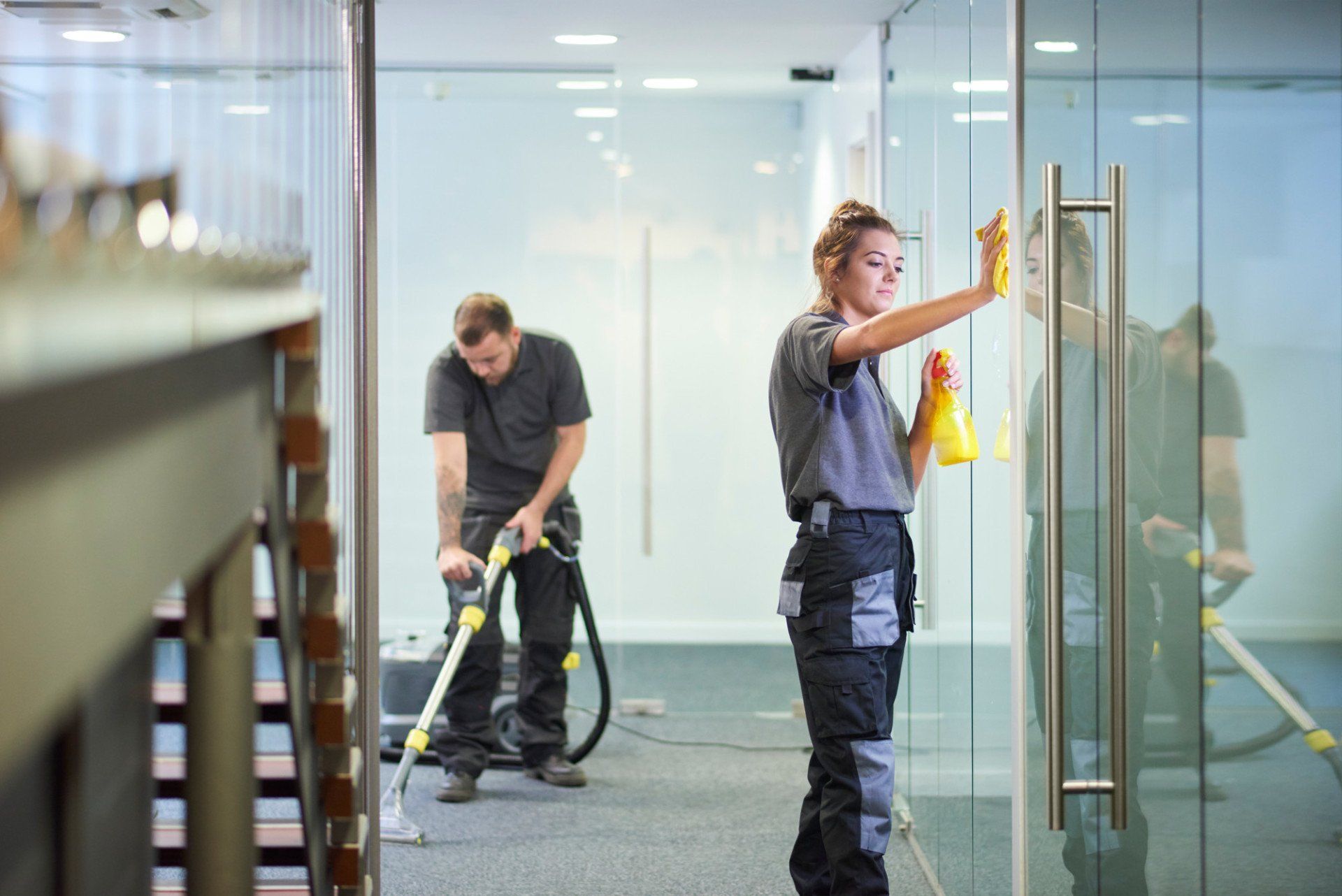 woman cleaning the office window, man cleaning floor using steam