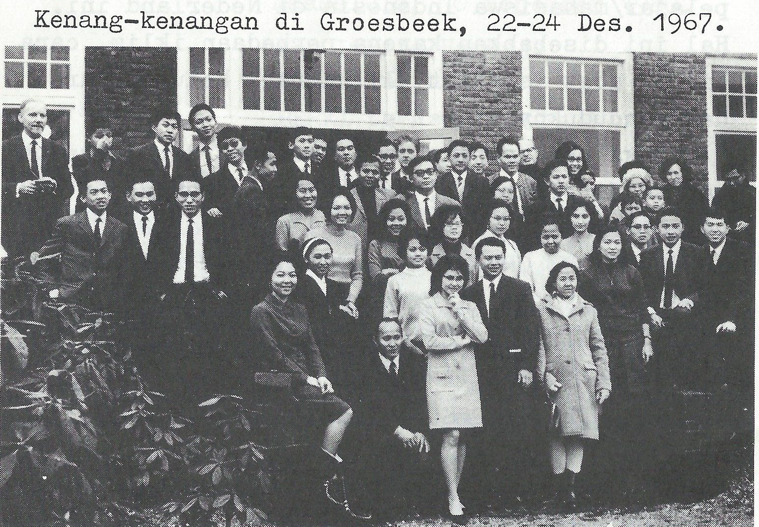 Groepsfoto voor een gebouw in Groesbeek, Nederland, december 1967. Veel mensen dragen formele kleding.