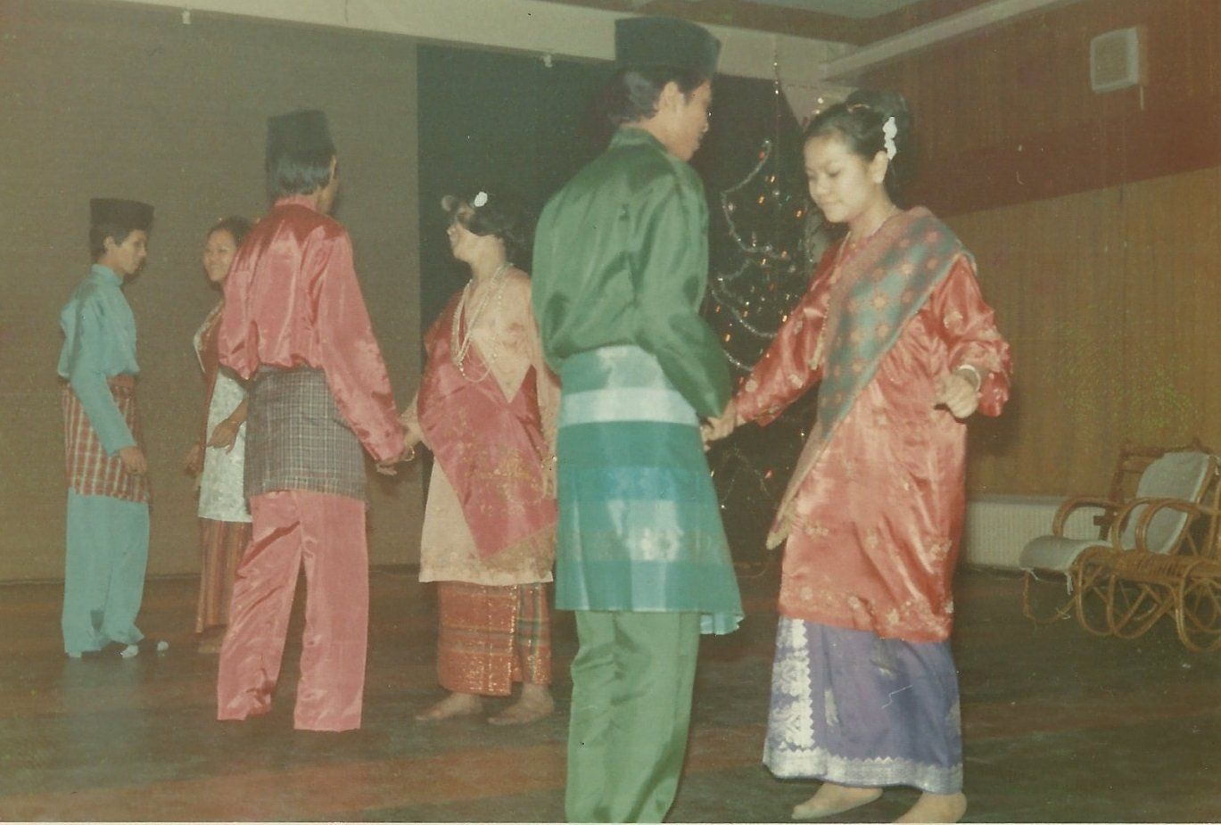 Mensen in traditionele Maleisische kleding dansen in een kamer.