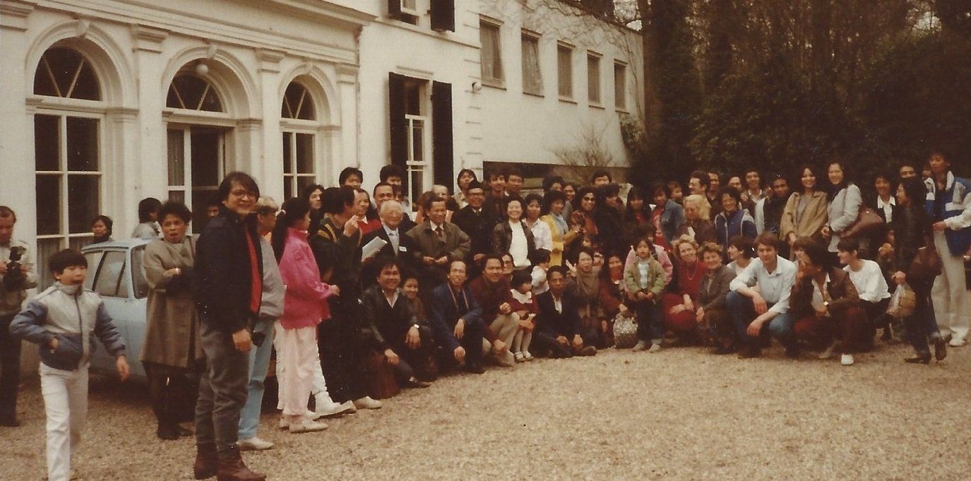 Een groep mensen poseert buiten voor een wit gebouw.