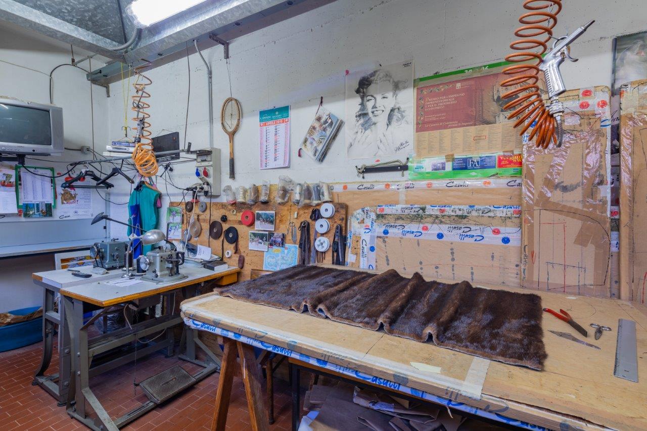 Un laboratorio per la riparazione di indumenti in pelliccia, con macchine da cucire, attrezzi e strisce di pelliccia marrone disposte su un tavolo di legno.