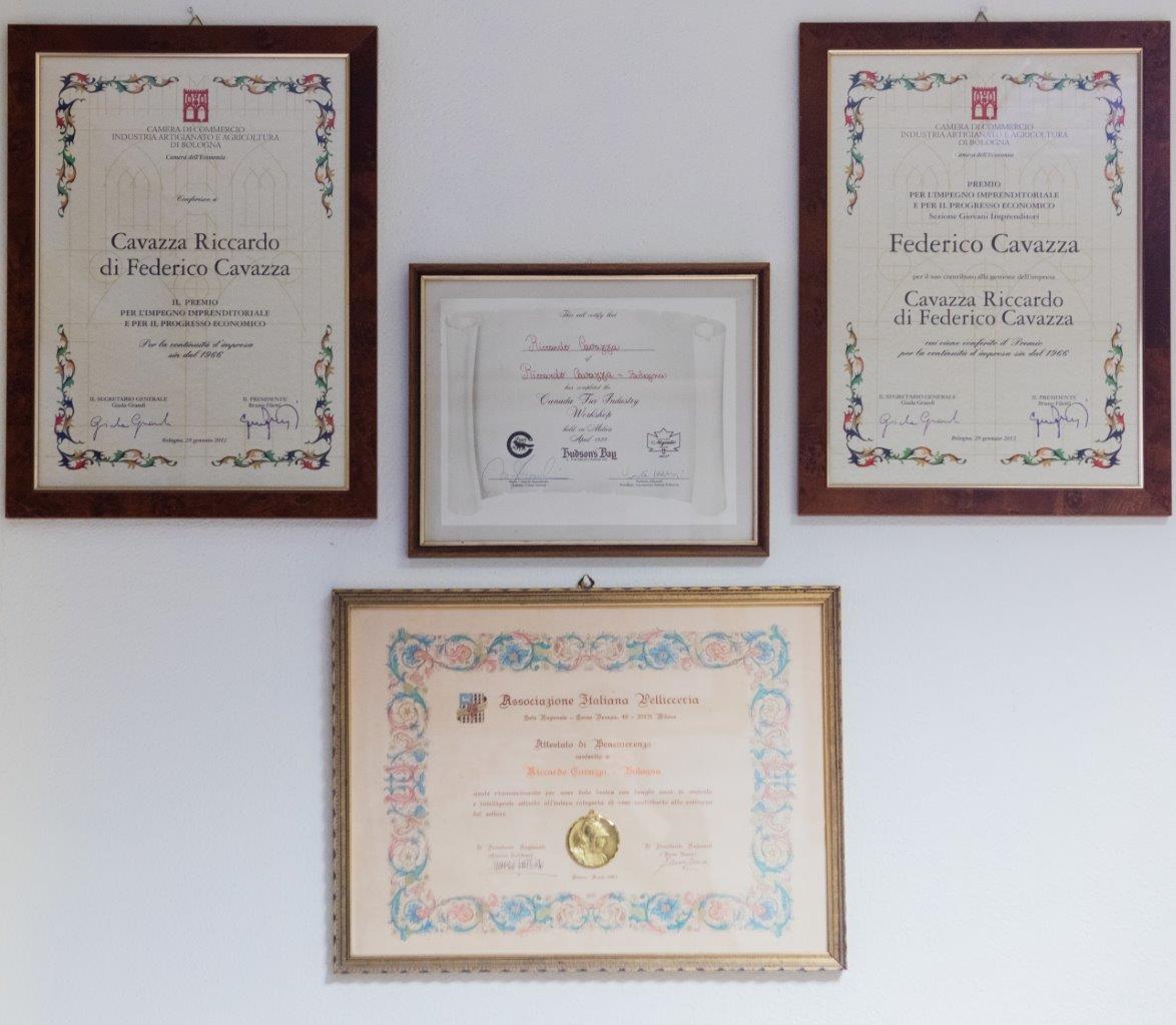 Su una parete bianca e spoglia sono appesi quattro certificati incorniciati, tre in alto e uno al centro in basso.