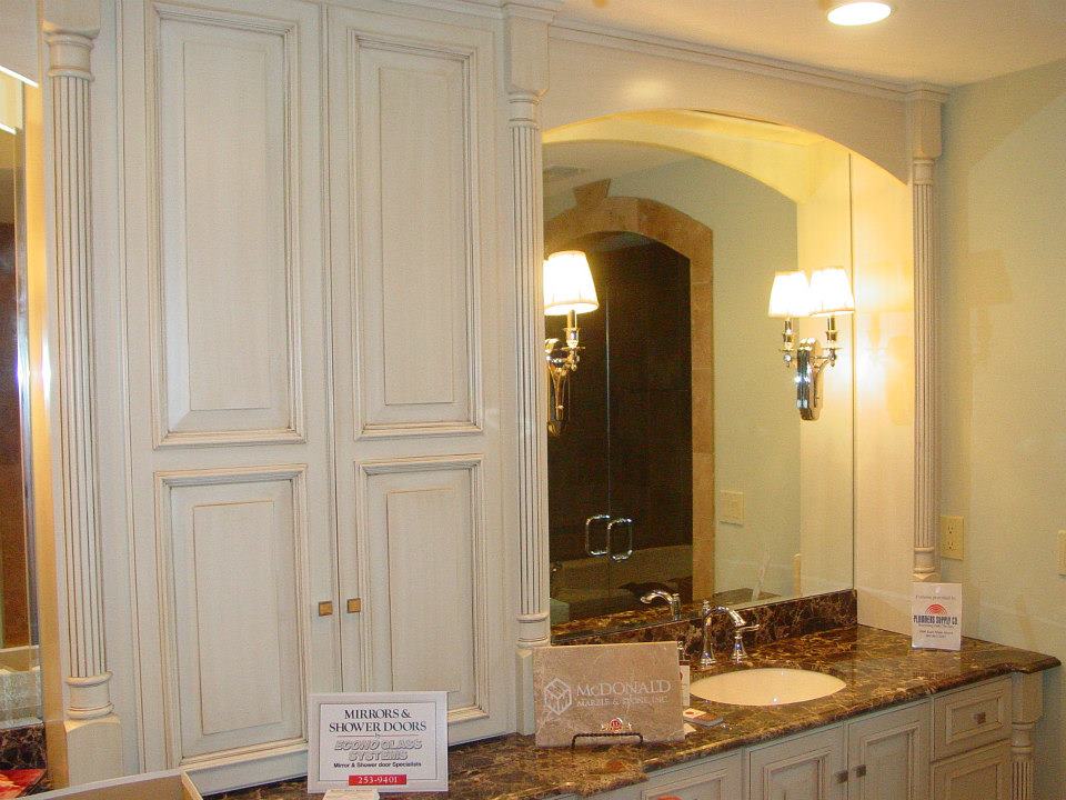 Bathroom vanity with cream cabinets, arched mirror, and dark granite countertop.