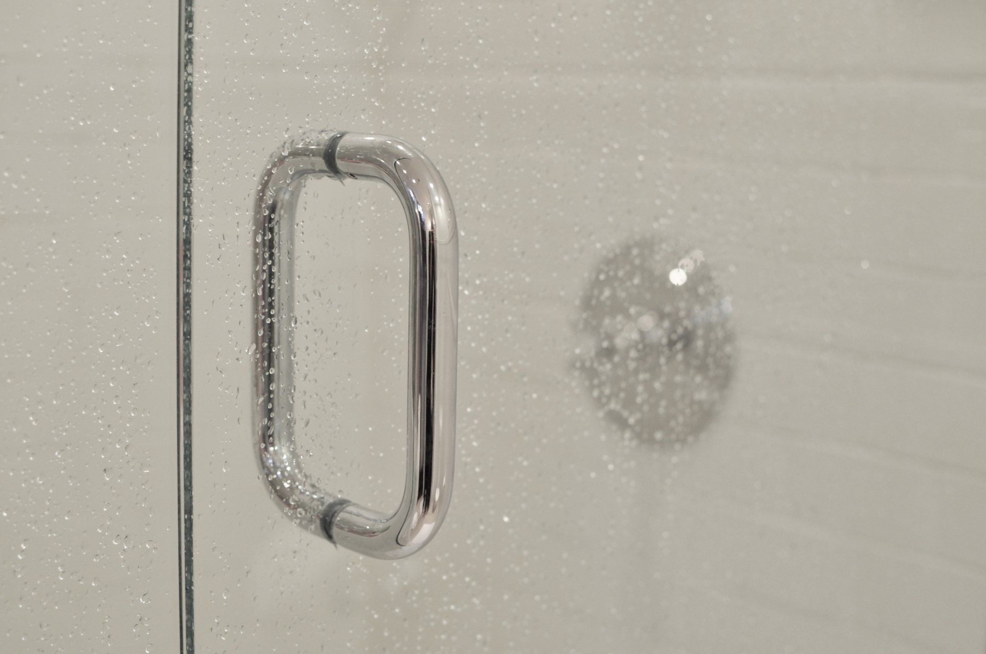 Close-up of a glass shower door handle with water droplets, showcasing modern bathroom design in Louisville, KY.